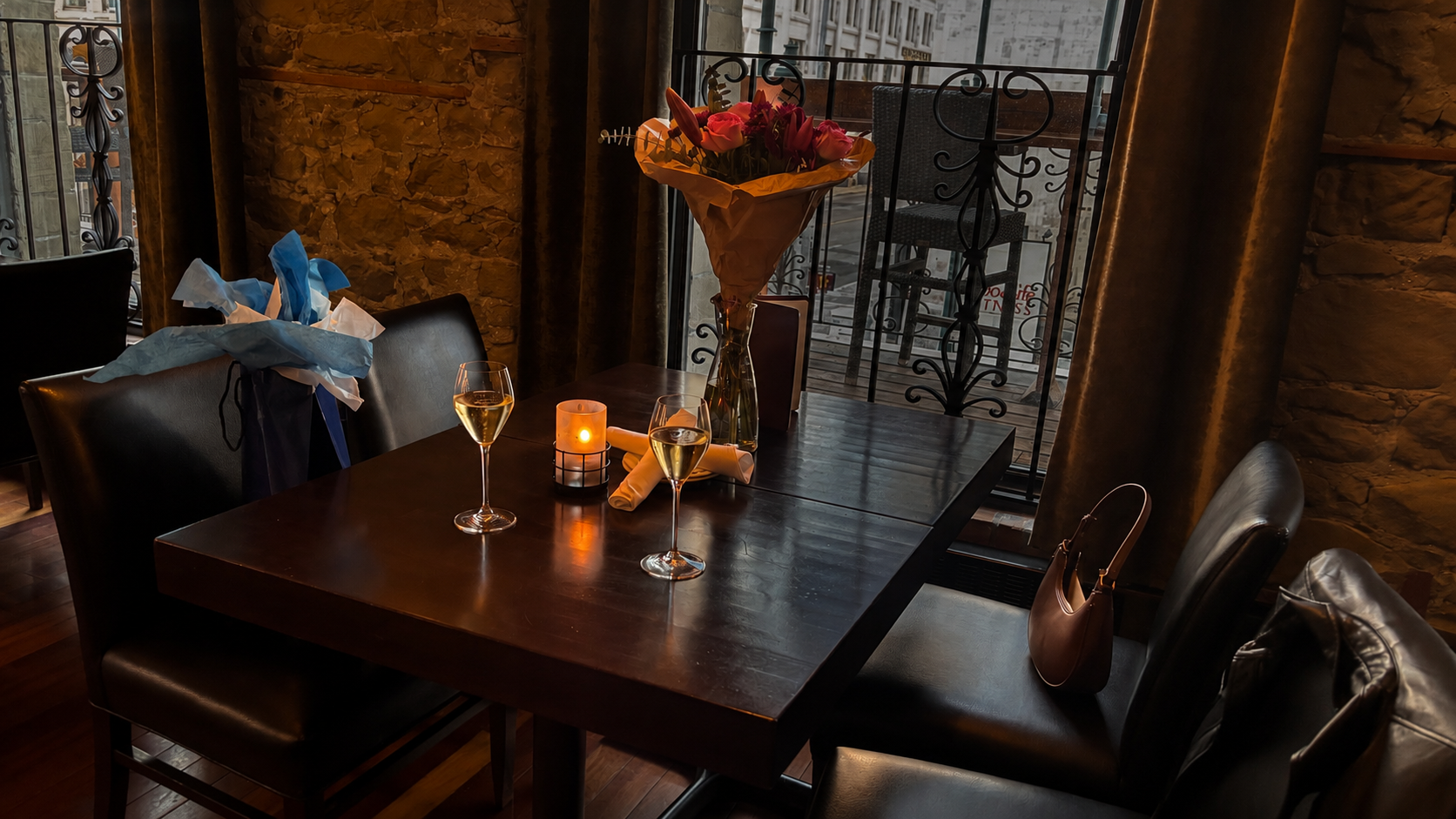 Candlelit restaurant table set for two with bubbles, flowers and a gift
